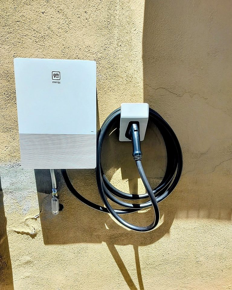 Level 2 home EV charger with coiled charging cable mounted on an exterior stucco wall
