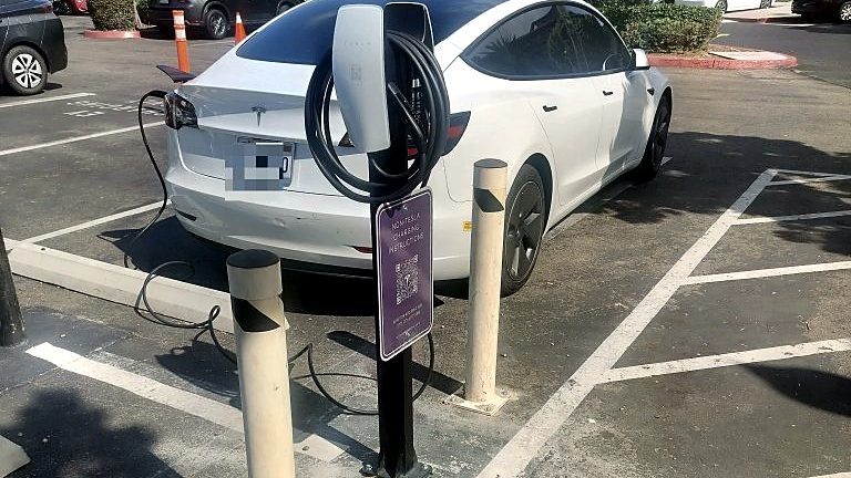 Tesla Model 3 plugged into a pedestal EV charging station in a parking lot